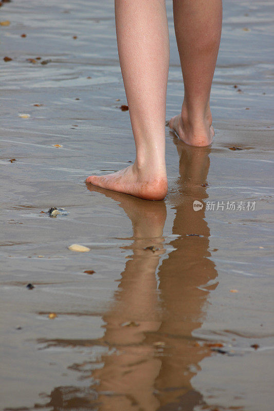 女孩走在潮湿的沙滩上，在沙滩/大海中倒影
